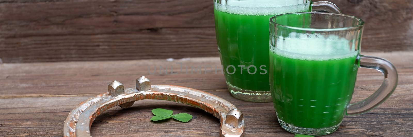 Shamrocks clovers on wooden table with a two mugs of green beer and a gold horseshoe. Background for St. Patrick's Day celebration