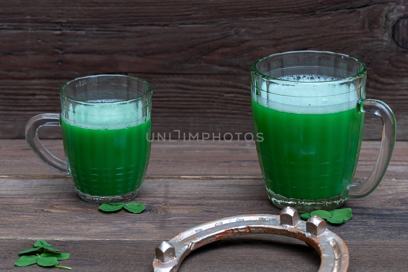 Shamrocks clovers on wooden table with a two mugs of green beer and a gold horseshoe. Background for St. Patrick's Day celebration