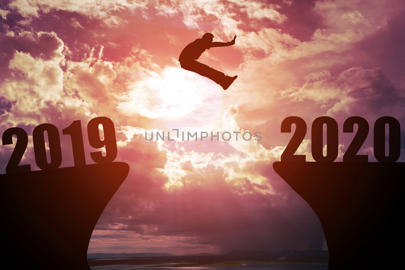 Silhouette of young business man jumping from the cliff that has the year number 2019 to the side that has the year number 2020 with sun rise background, Concept for new year target.