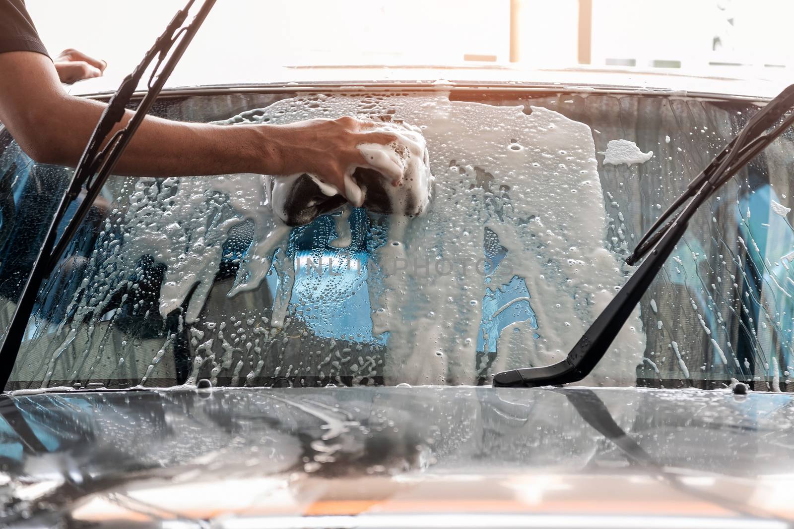 The car wash staff is using a sponge to clean the windshield of the car.