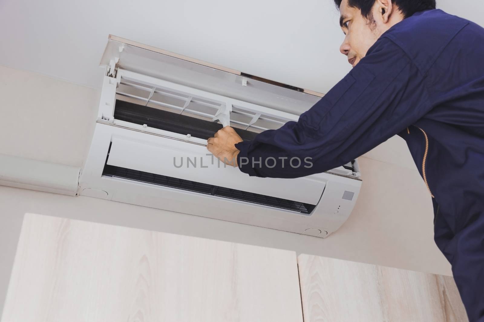 Air mechanic repairman in blue uniform is checking the air conditioner hanging on the wall.