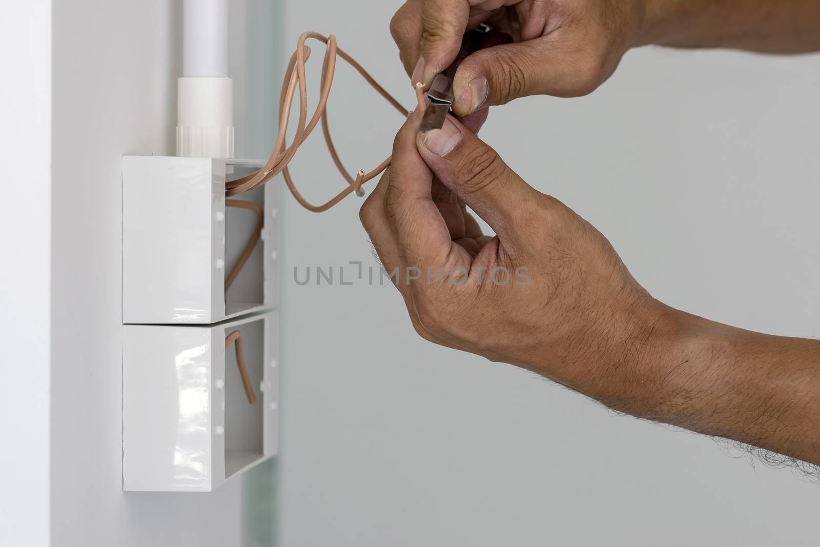 The electrician is using a knife to cut the wire to install the power switch in the box on the wall.