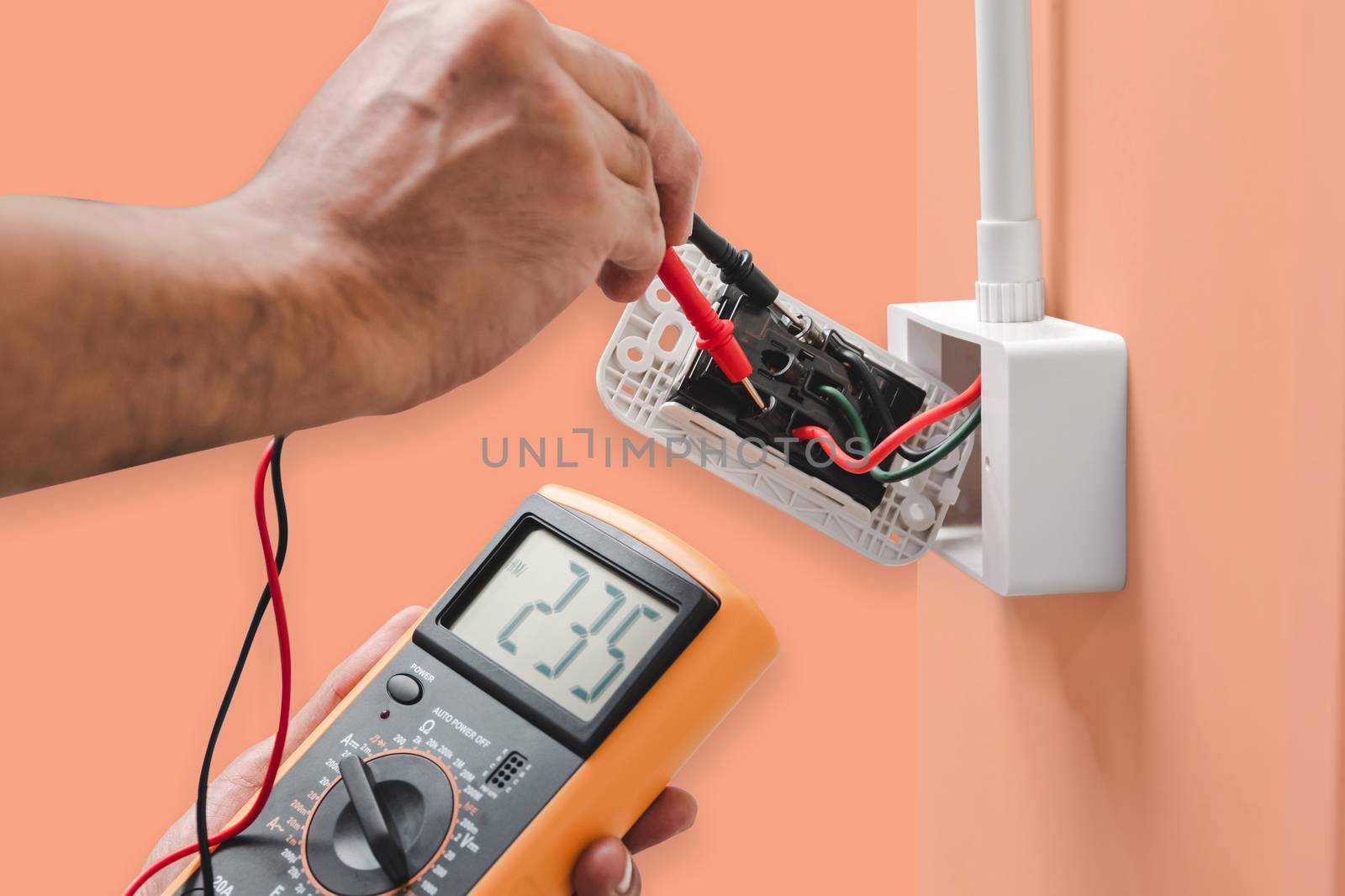 Electrician is using a digital meter to measure the voltage at the power outlet  isolated on orange color pastel background, with clipping path.