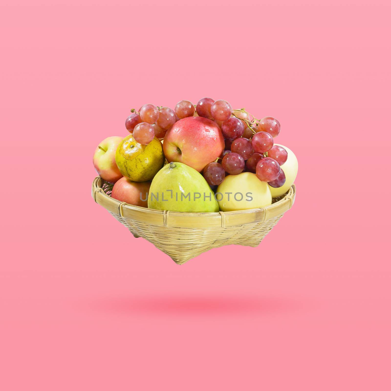 Group of many fruits in a bamboo basket isolated on beautiful pink color pastel background, with clipping path.