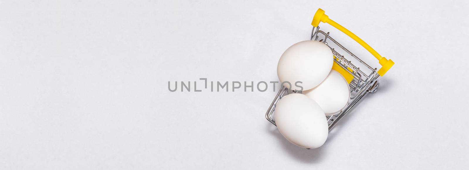 Fresh eggs in a shopping cart. Top view. Shopping, purchasing, and food delivery concept. White background. Close up shot. Isolated. Panorama, banner size with copy space.