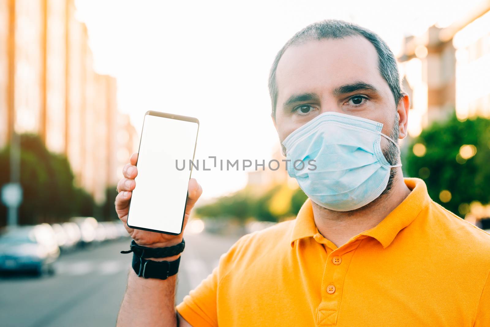 Portrait of 40s aged man with surgical medical mask standing, holding and showing smart phone display. by Fotoeventis