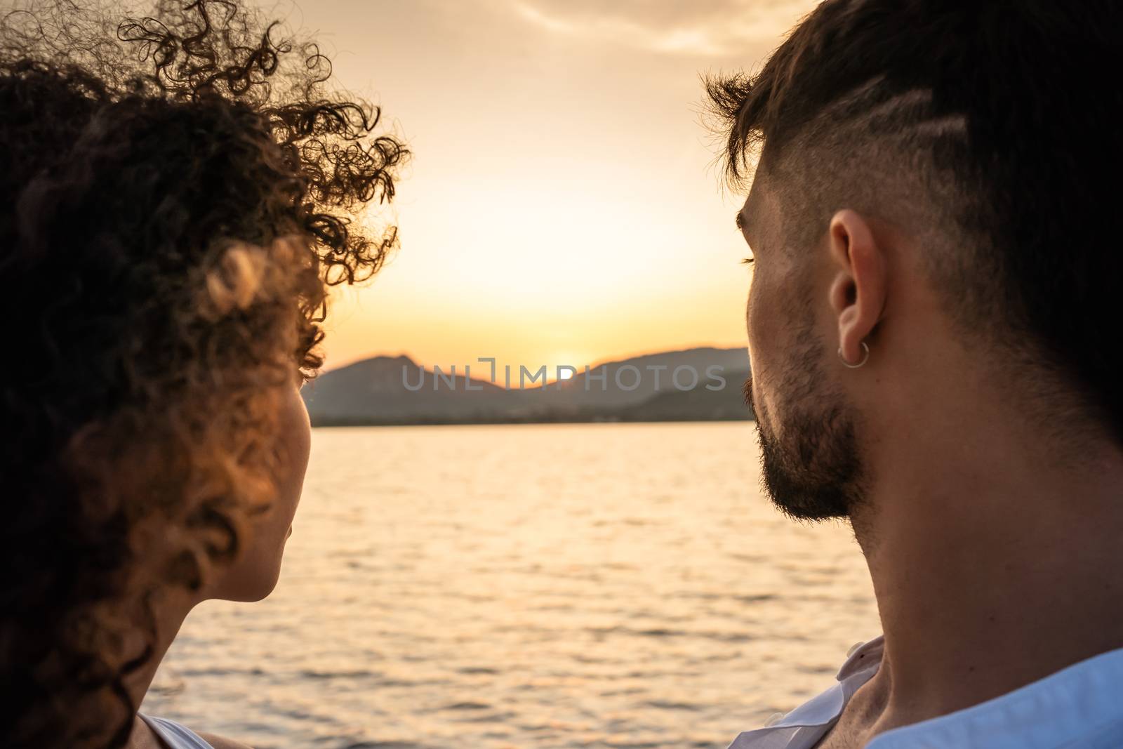 Romantic beautiful mixed race couple close-up with setting sun in center of the photography - Back view of stylish modern young man and his hispanic cute girlfriend looking at the sunset
