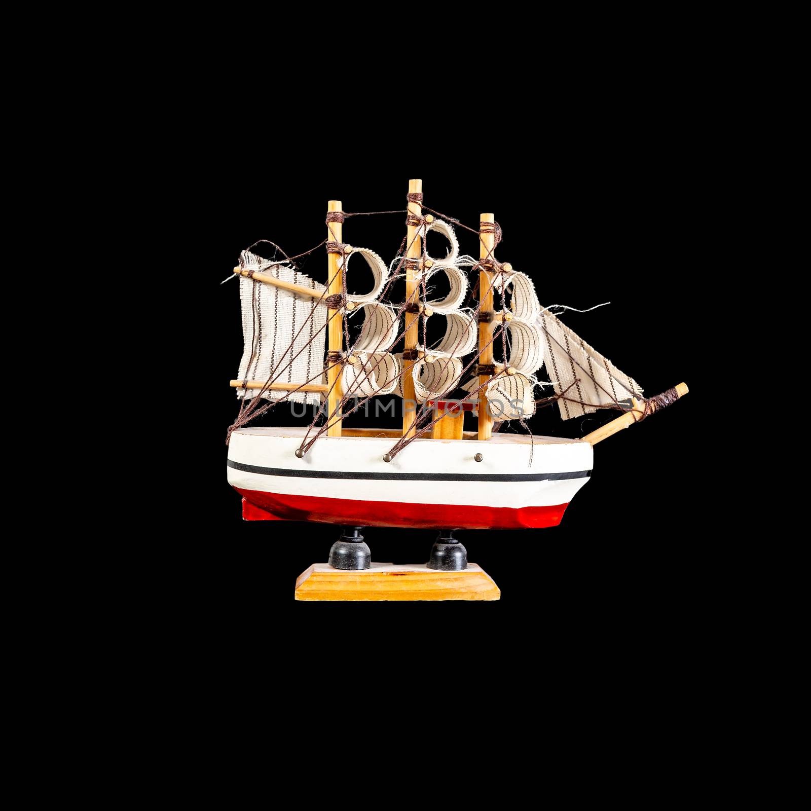 Toy boat sailboat on a wooden stand isolated on a black background. Model of the ship with a red stripe. side view