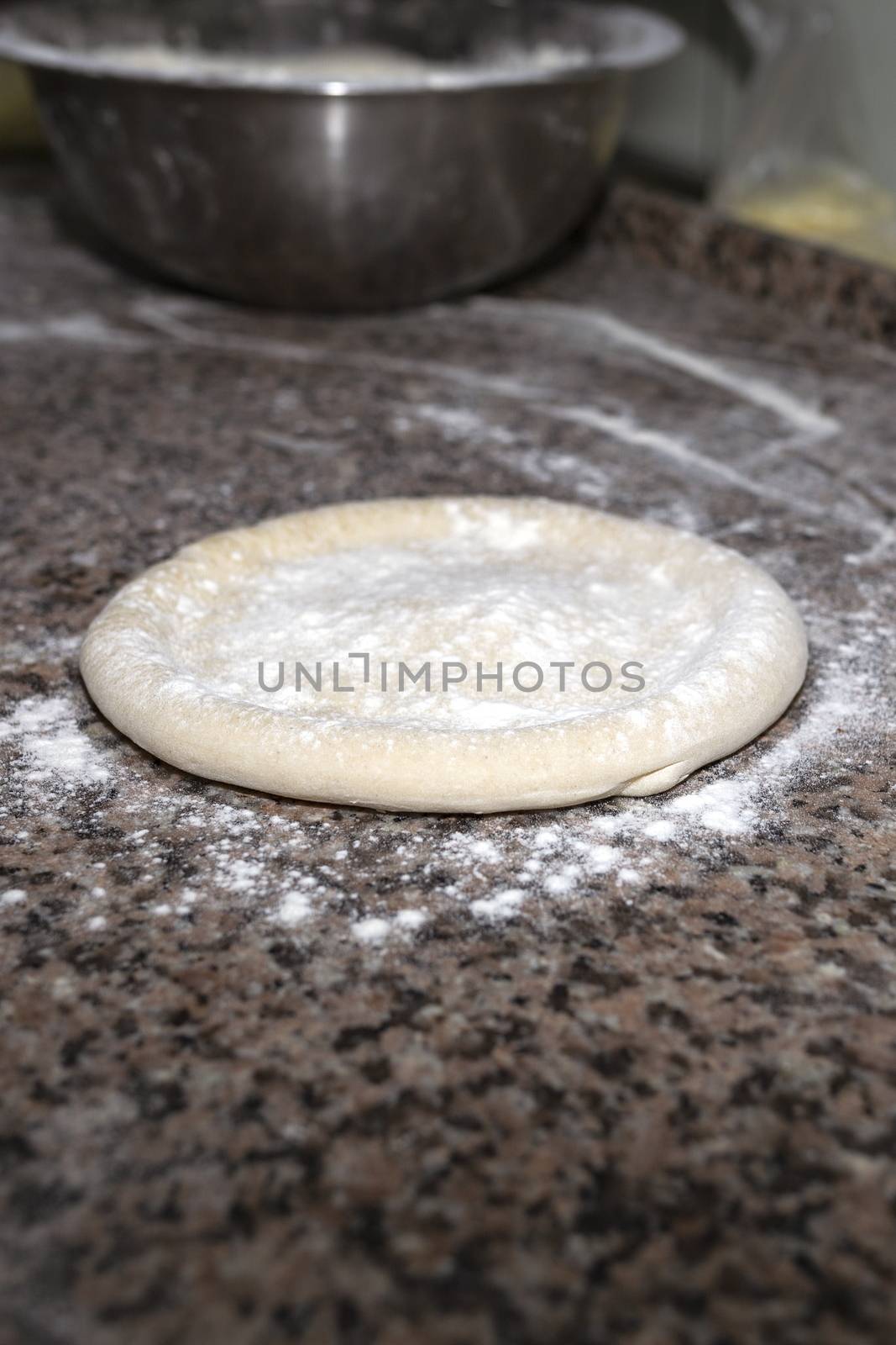 Pizza raw dough floured lies on granite table. Dough preparation for Italian pizza. Cooking food. Vertical image