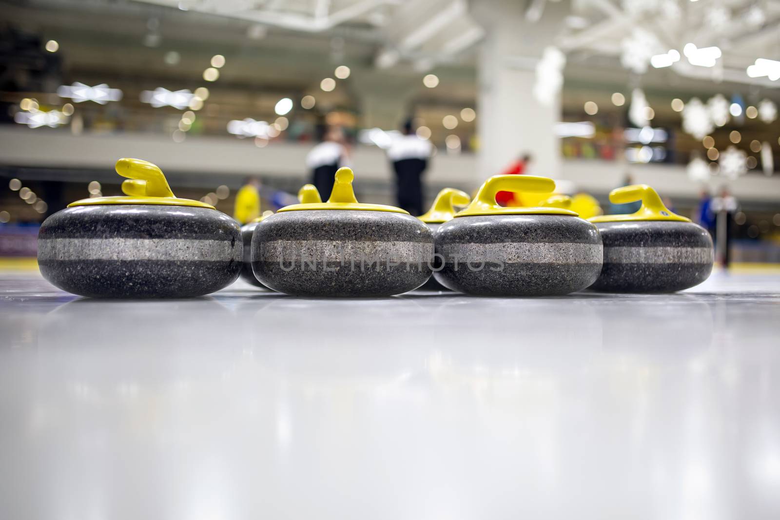 The curling stone or rock is made of granite with yellow handles lie on the ice