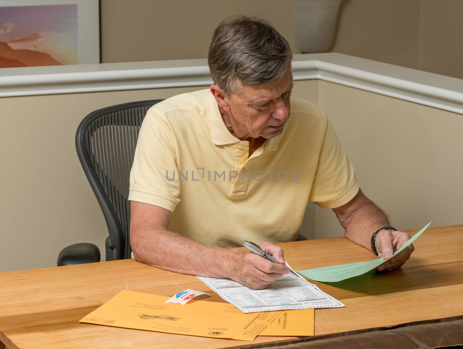 Senior caucasian man seated at home desk and completing the mail-in or absentee ballot for the 2020 presidential election