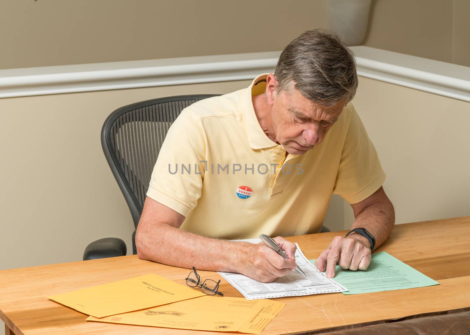 Senior caucasian man sitting at his desk and completing absentee voting ballot by steheap