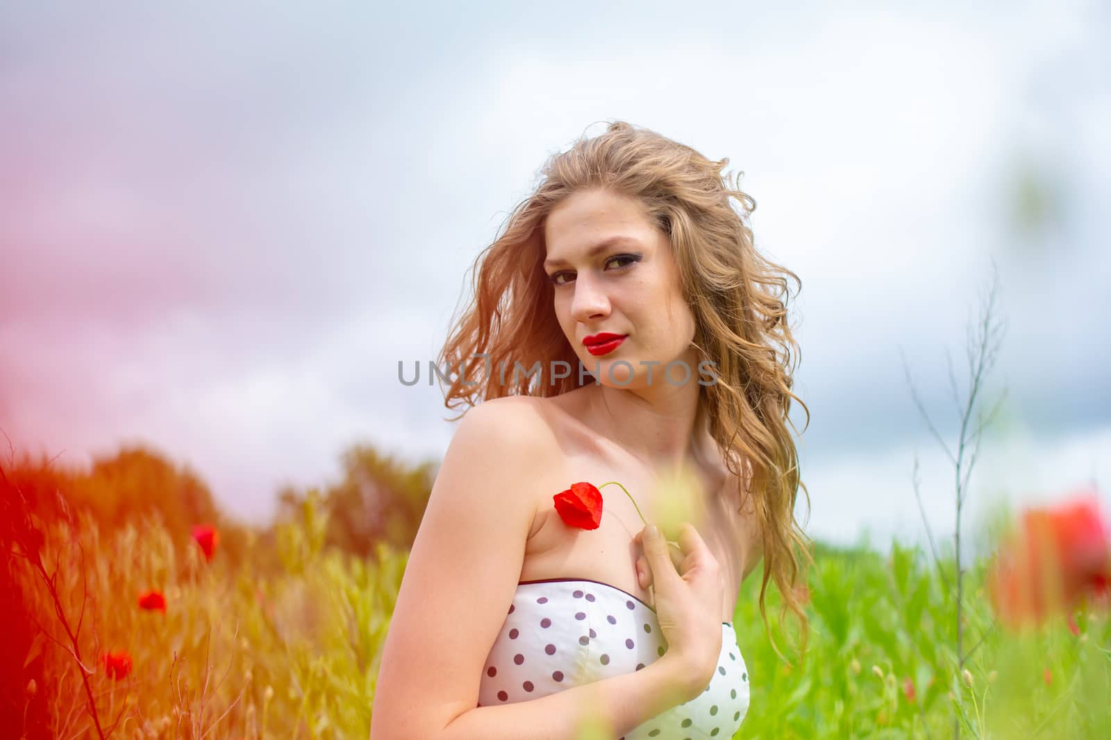 A young long-haired girl enjoys the colors of nature on a blooming poppy field on a hot summer day by Try_my_best
