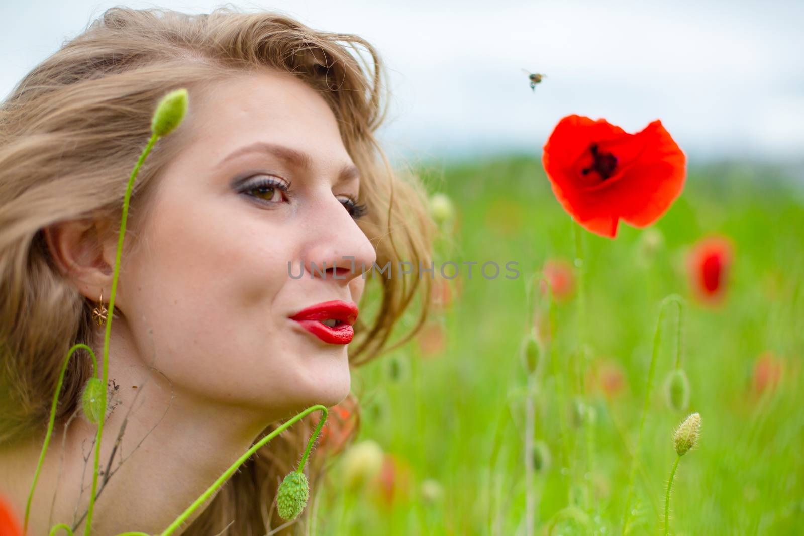 A young long-haired girl enjoys the colors of nature on a blooming poppy field on a hot summer day by Try_my_best