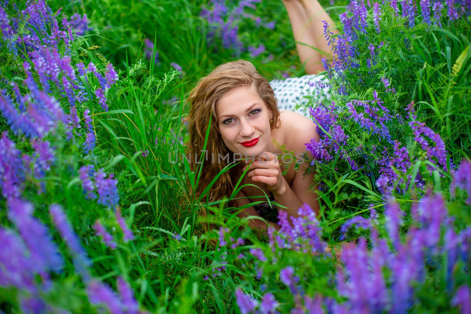 Beautiful young blonde girl in a green field among purple wildflowers. Wildlife beautiful girl.