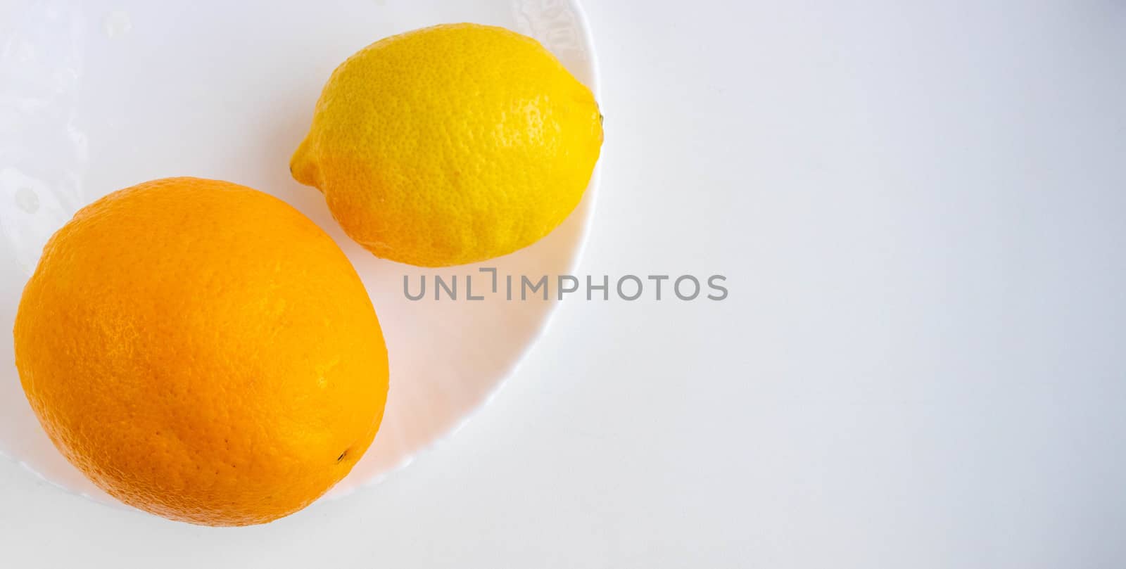 One lemon and an orange lie on a white plate, isolated on a white background. Tropical fruit. Flat bed, top view.