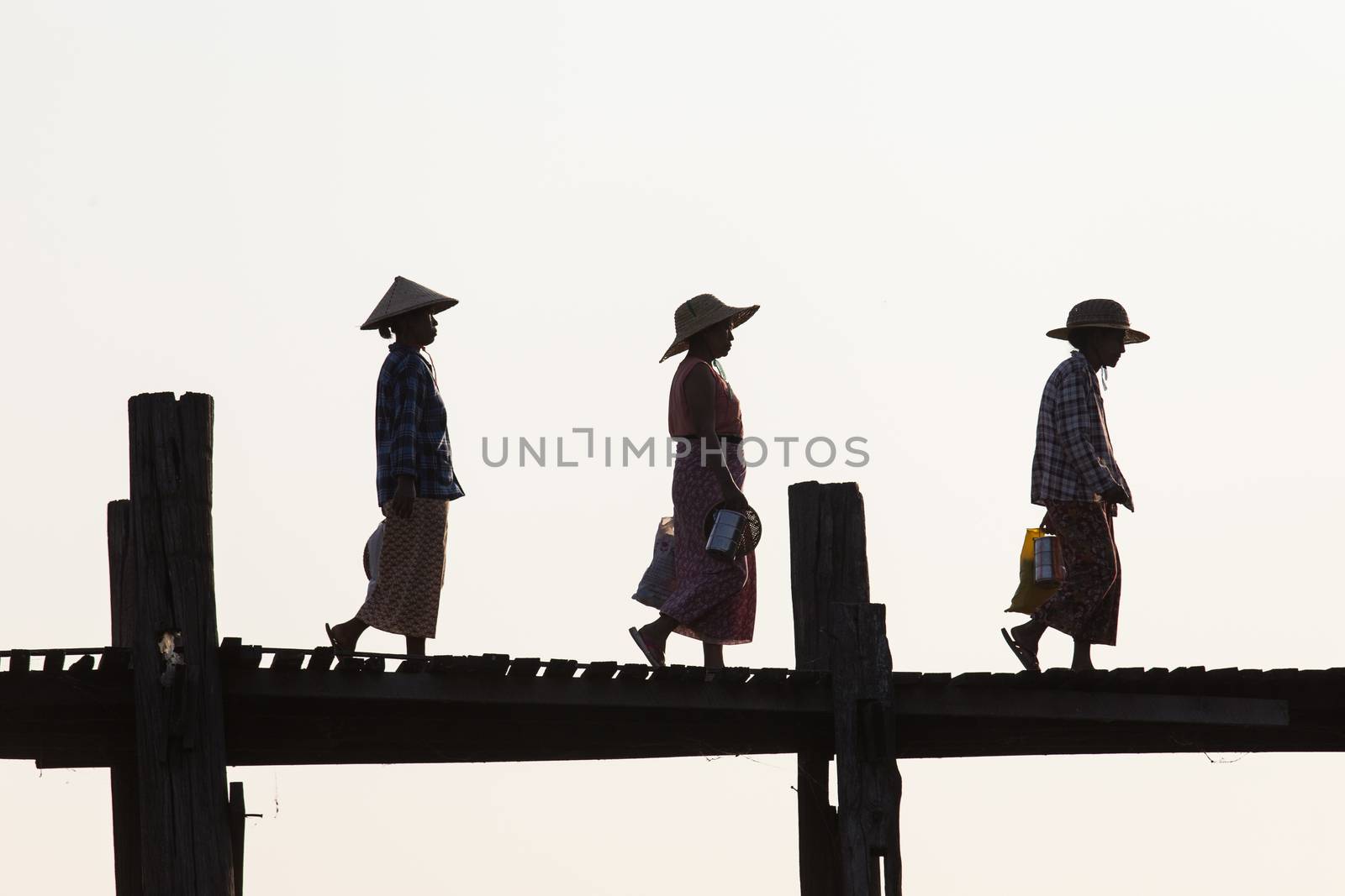 Silhouettes of local women in hats walking on u bien bridge Mandalay, Myanmar by kgboxford