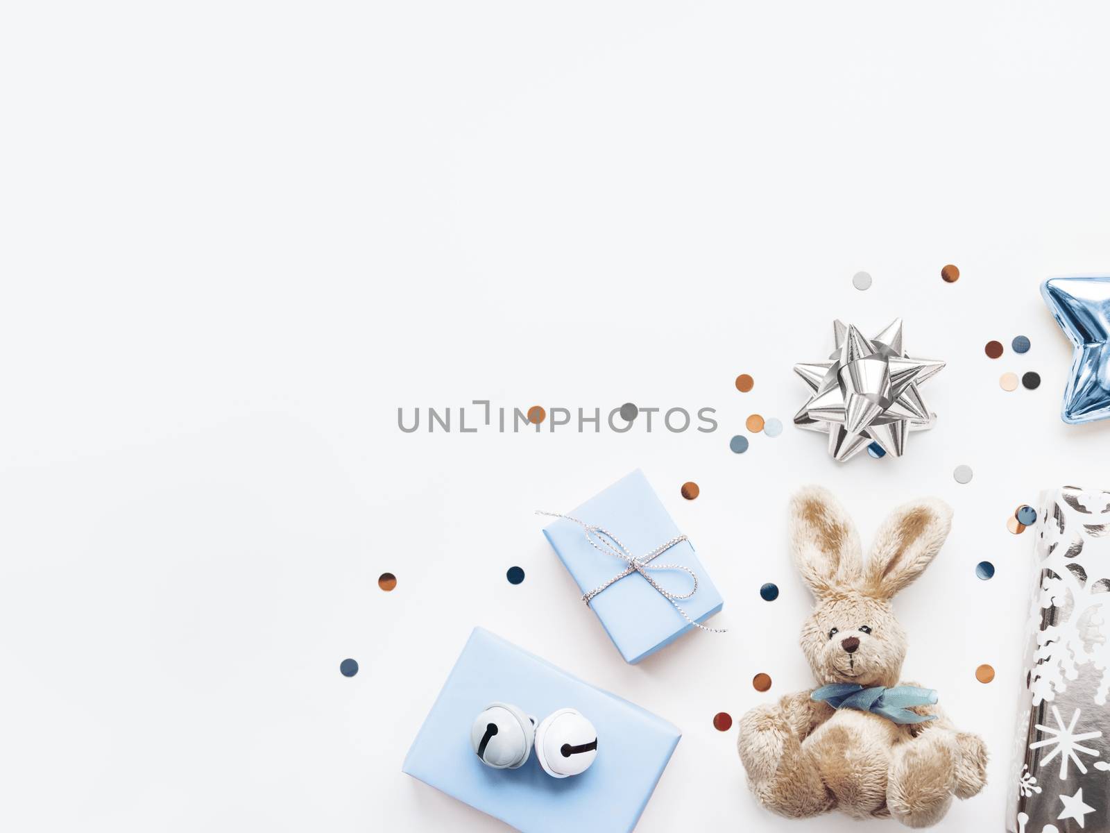 Holiday presents in shadows of blue - fluffy toy rabbit, gifts with decorative bells, sparkling confetti, decorative star. Gifts for little boy on Birthday.