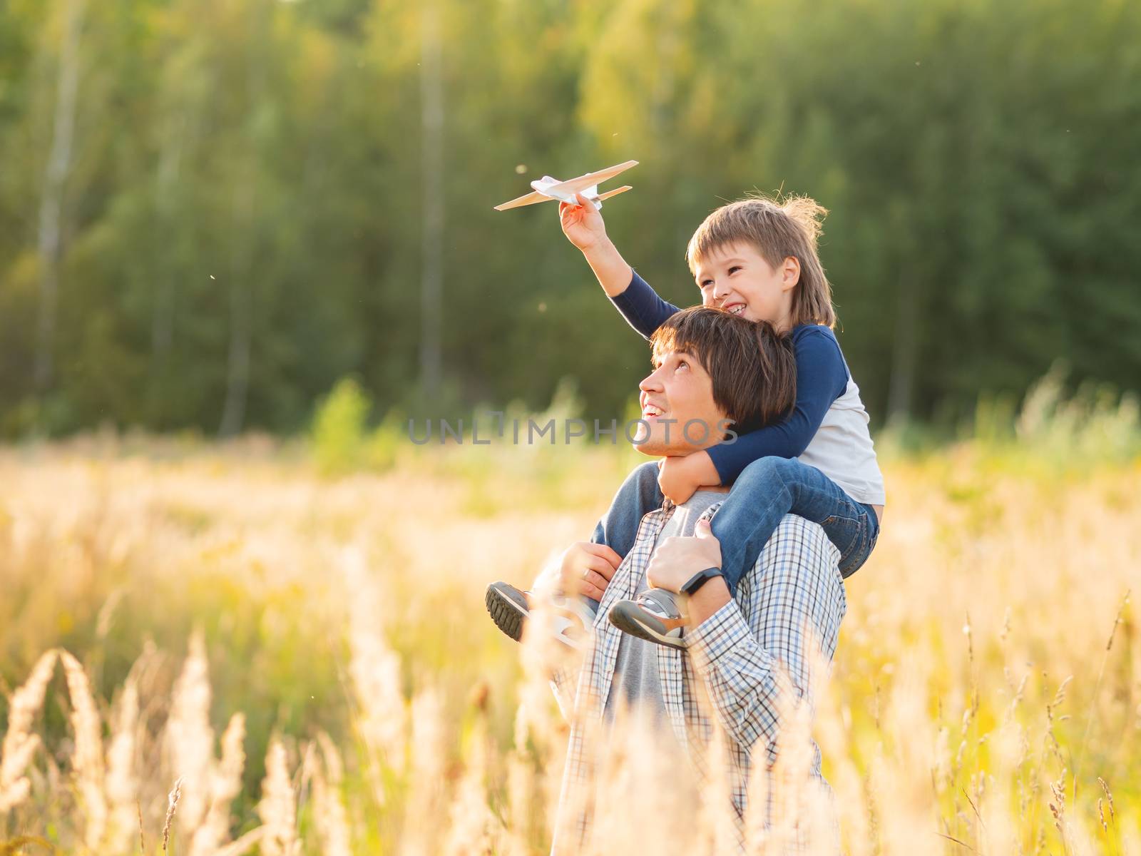 Cute boy and his father play with toy air plane. Happy kid dreams to be a pilot. Boy is planning for the future. Dad and son on field at golden sunset hour at autumn season.