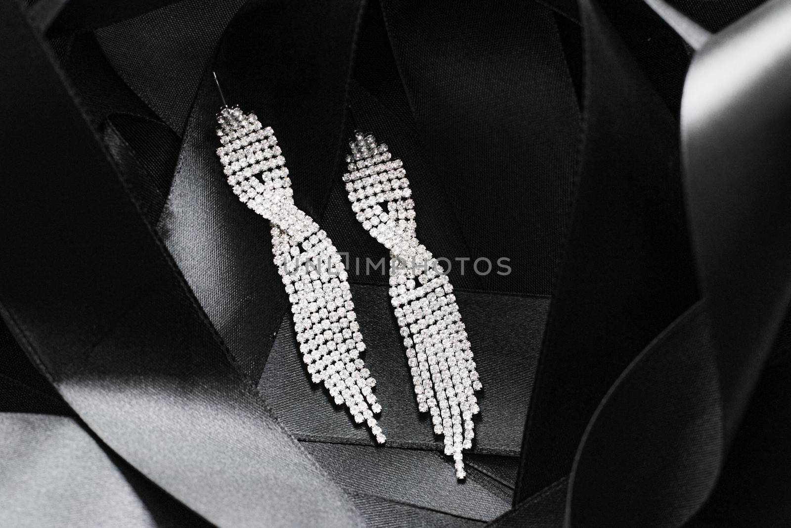 Luxury diamond earrings on black silk ribbon as background, jewelry and fashion brands