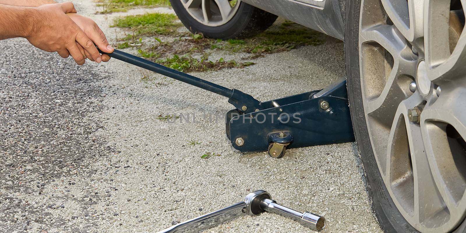 Man changing wheel. tire changer changing flat car tire. Help on road concept. Mechanic hands unscrews a flat tire of a car raised on a jack by PhotoTime