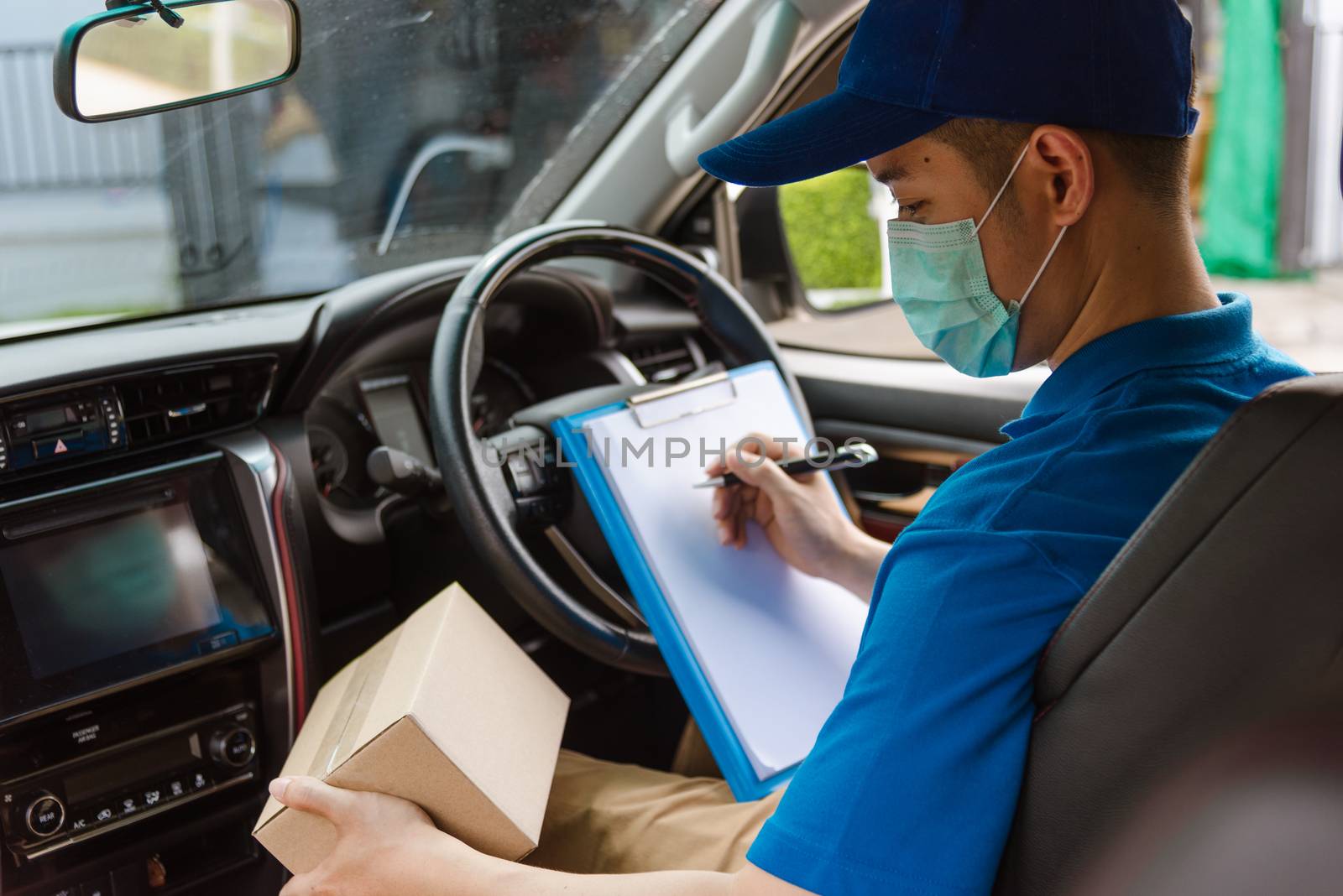 Asian delivery courier young man driver inside the van car with parcel post boxes checking amount he protective face mask, under curfew quarantine pandemic coronavirus COVID-19