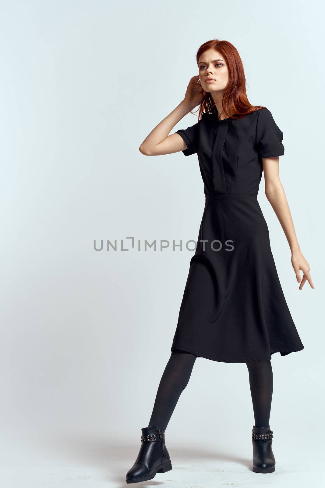 A woman in a black dress on a light background and pantyhose shoes red hair and pose in full growth by SHOTPRIME