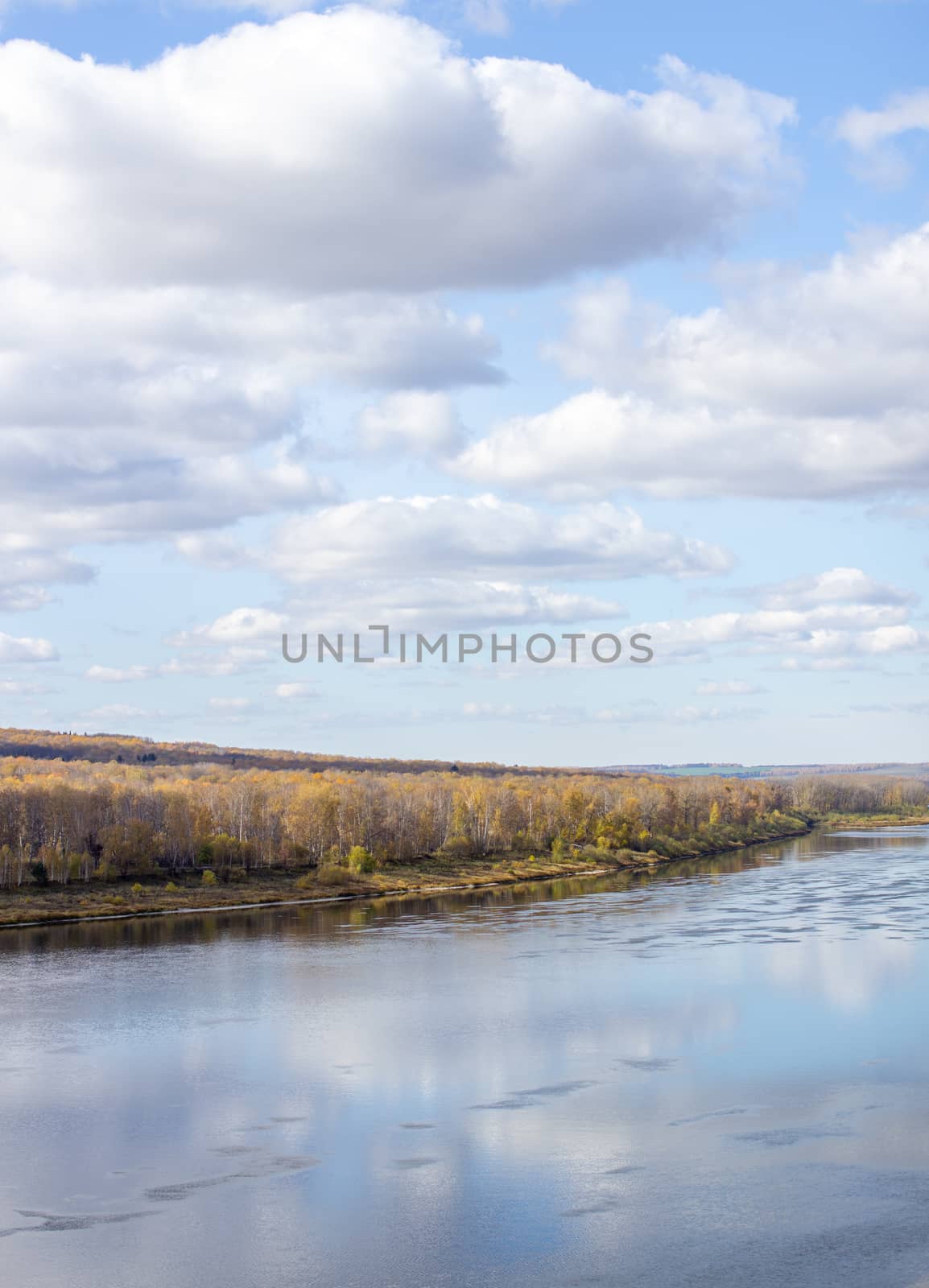 Beautiful, wide river autumn among the woods. Calm and quiet place with autumn colors. Reflection of clouds and forests in water in good weather