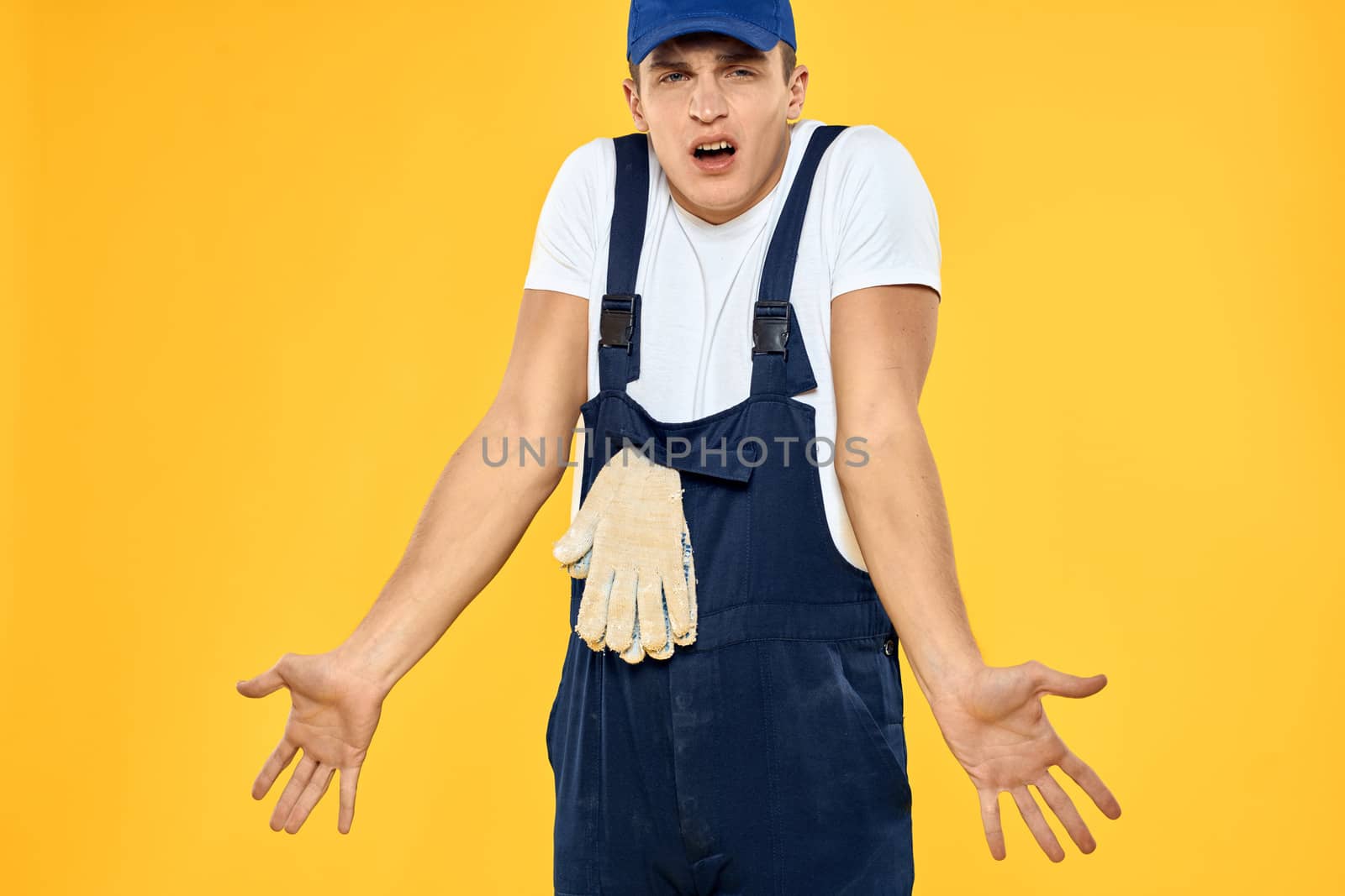 Working man in uniform of gloves rendering service yellow background. High quality photo