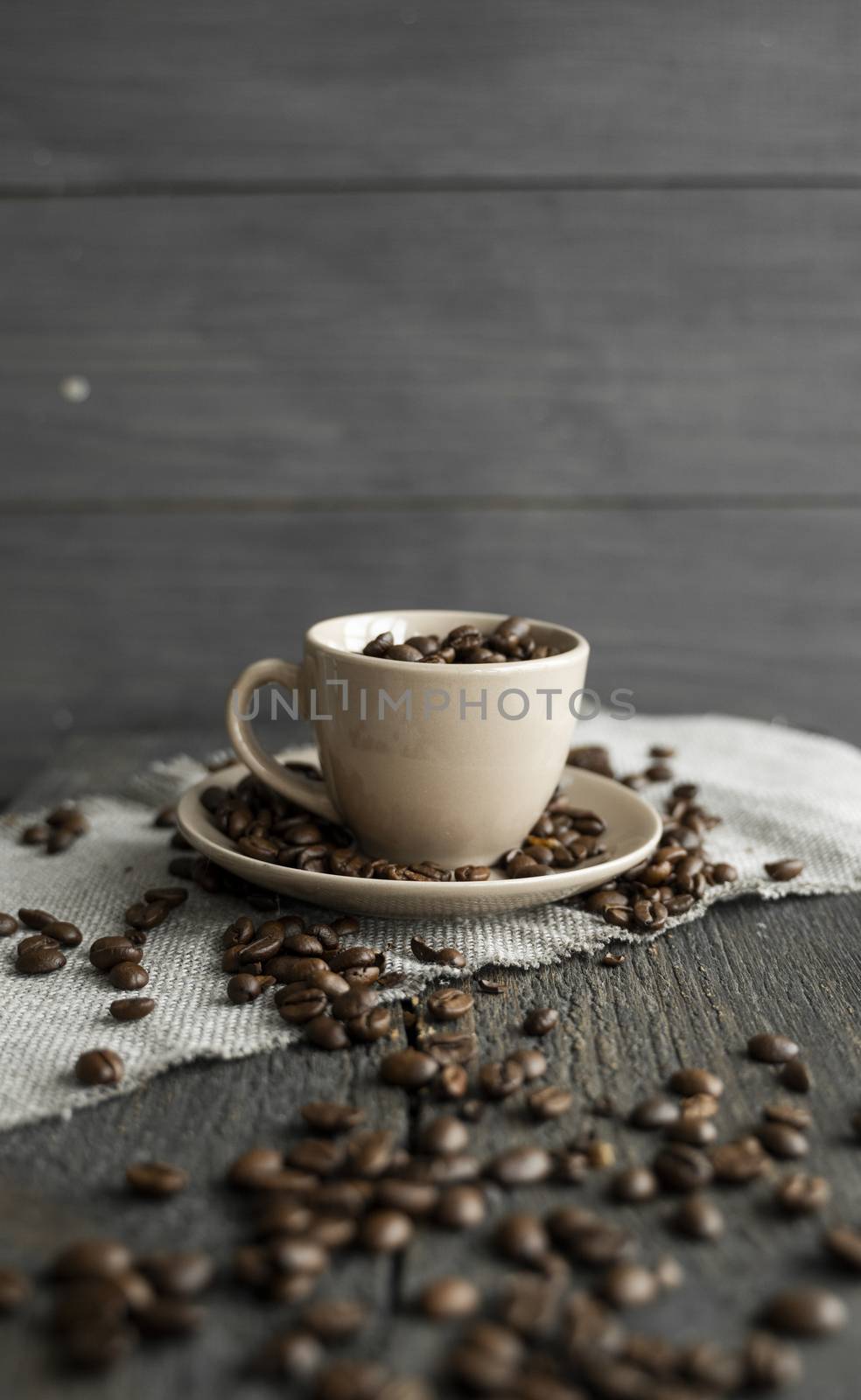 Coffee cup filled of fresh arabica or robusta coffee beans with scattered coffee beans on a linen textile and wood table