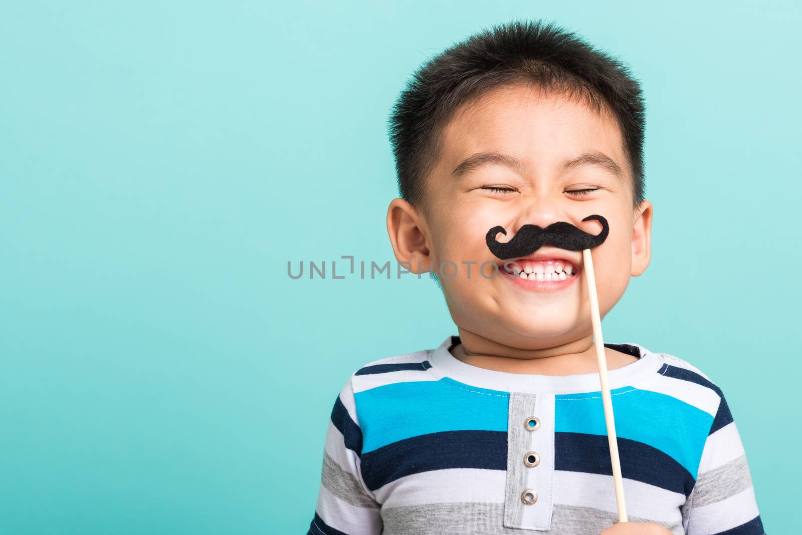 Funny happy hipster kid holding black mustache props for the photo booth close face, studio shot isolated on a blue background, Men health awareness, Prostate Cancer Awareness