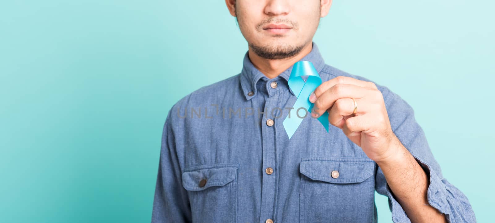 Asian portrait happy handsome man posing he holding light blue ribbon for supporting people living and illness, studio shot isolated on blue background, Prostate Cancer Awareness in November concept