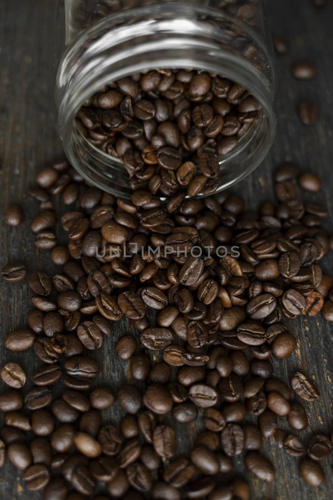 Roasted fresh arabica coffee beans scattered on a table from a little jar on a wooden table. Fresh coffee beans