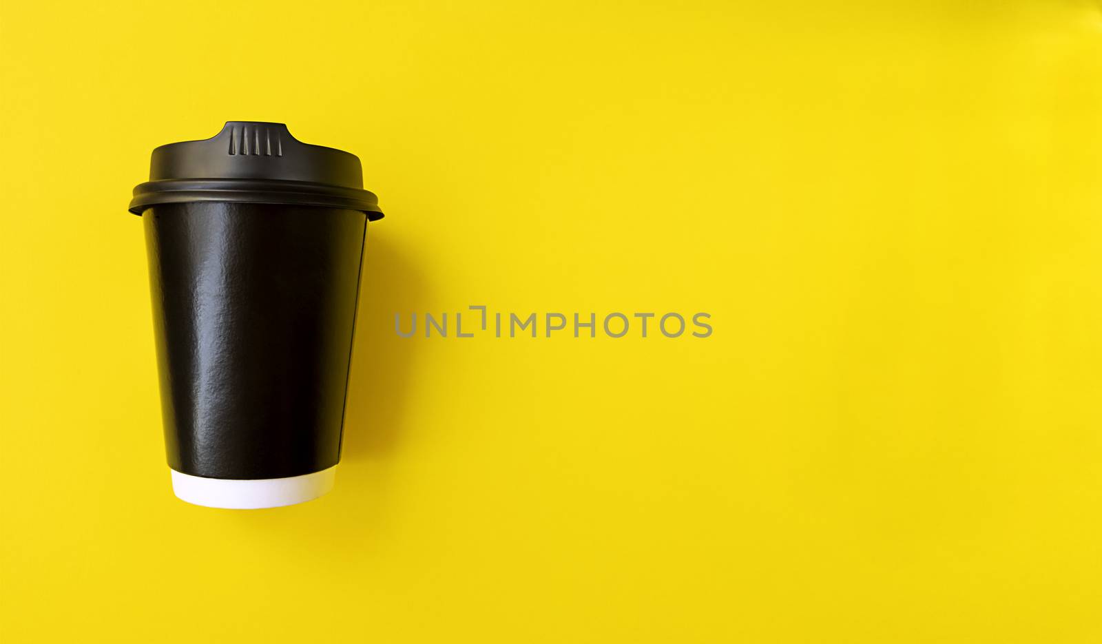 Black paper coffee cup to go on yellow backgroud. Simple flat lay with copy space. Minimal concept. Stock photo.