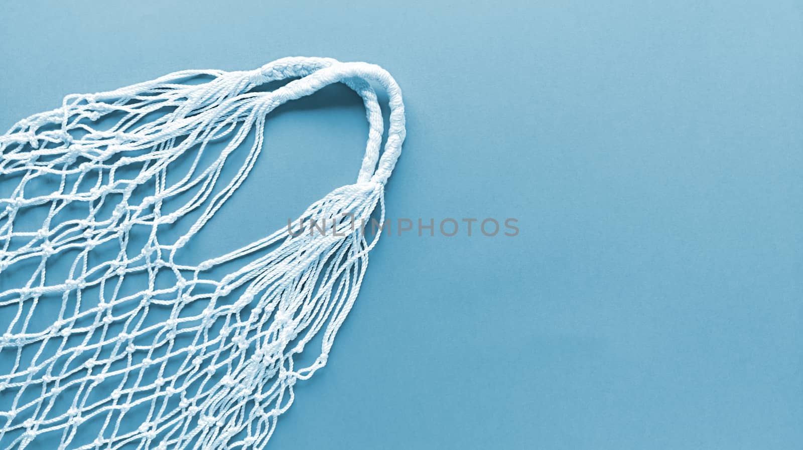 White string cotton eco bag on a blue background. Monochrome simple flat lay with copy space. Ecology zero waste concept. Stock photography.