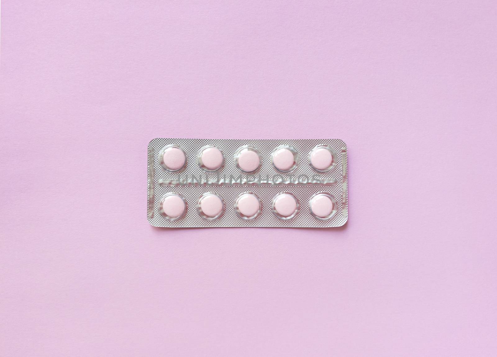 A blister of soft pink pills in the middle on pink background. Monochrome simple flat lay with pastel texture. Medical concept. Stock photography.
