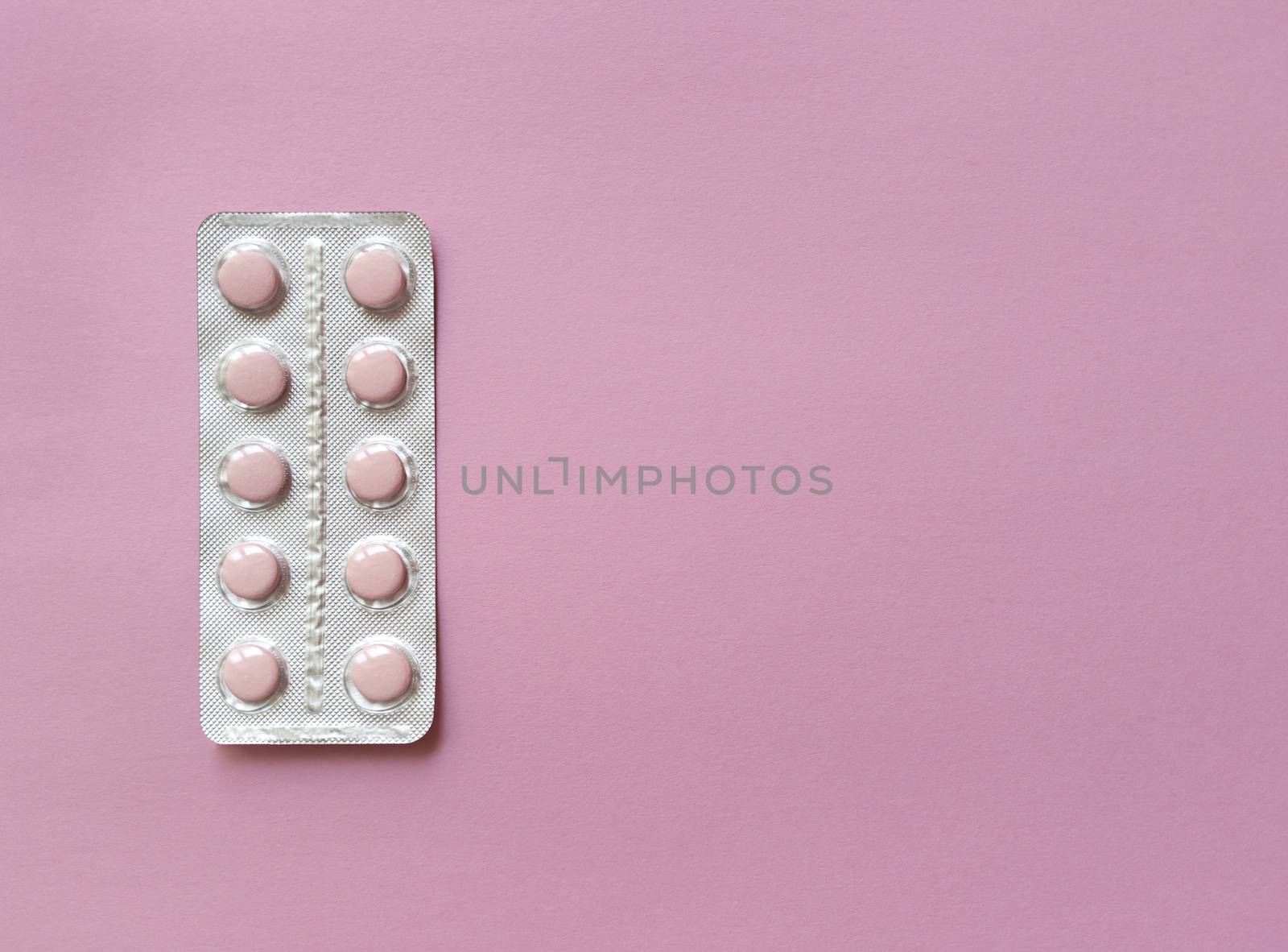 A blister of soft pink pills on pink background. Monochrome simple flat lay with pastel texture with copy space. Medical concept. Stock photography.