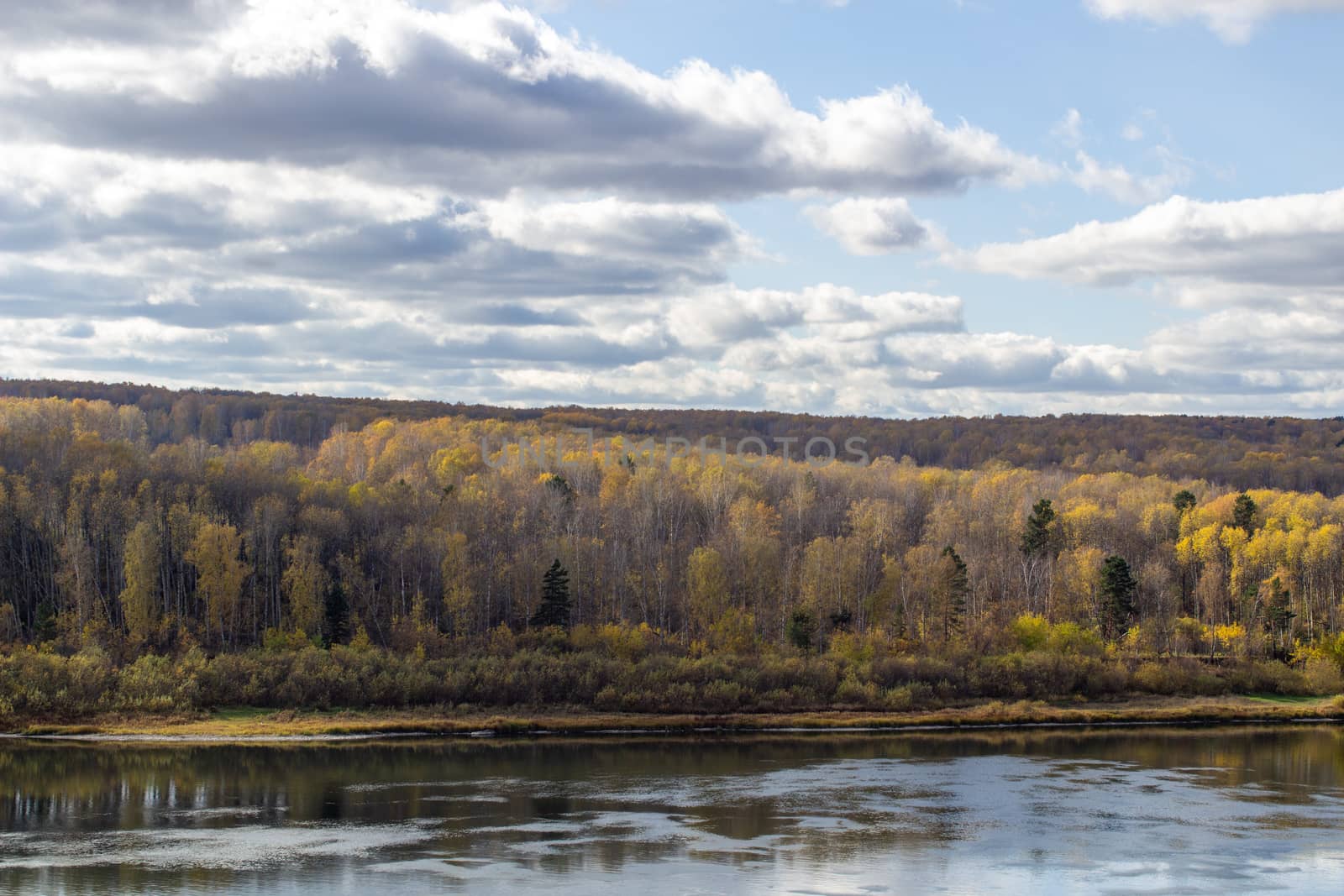 Beautiful, wide river autumn among the woods. Calm and quiet place with autumn colors. Reflection of clouds and forests in water in good weather