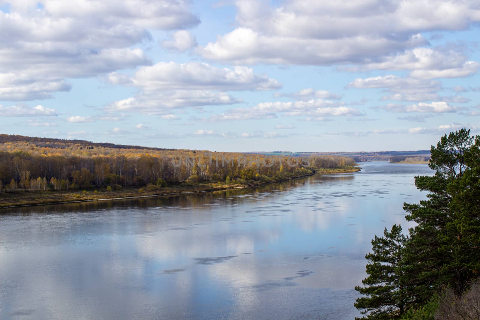 Beautiful, wide river autumn among the woods. Calm and quiet place with autumn colors. Reflection of clouds and forests in water in good weather
