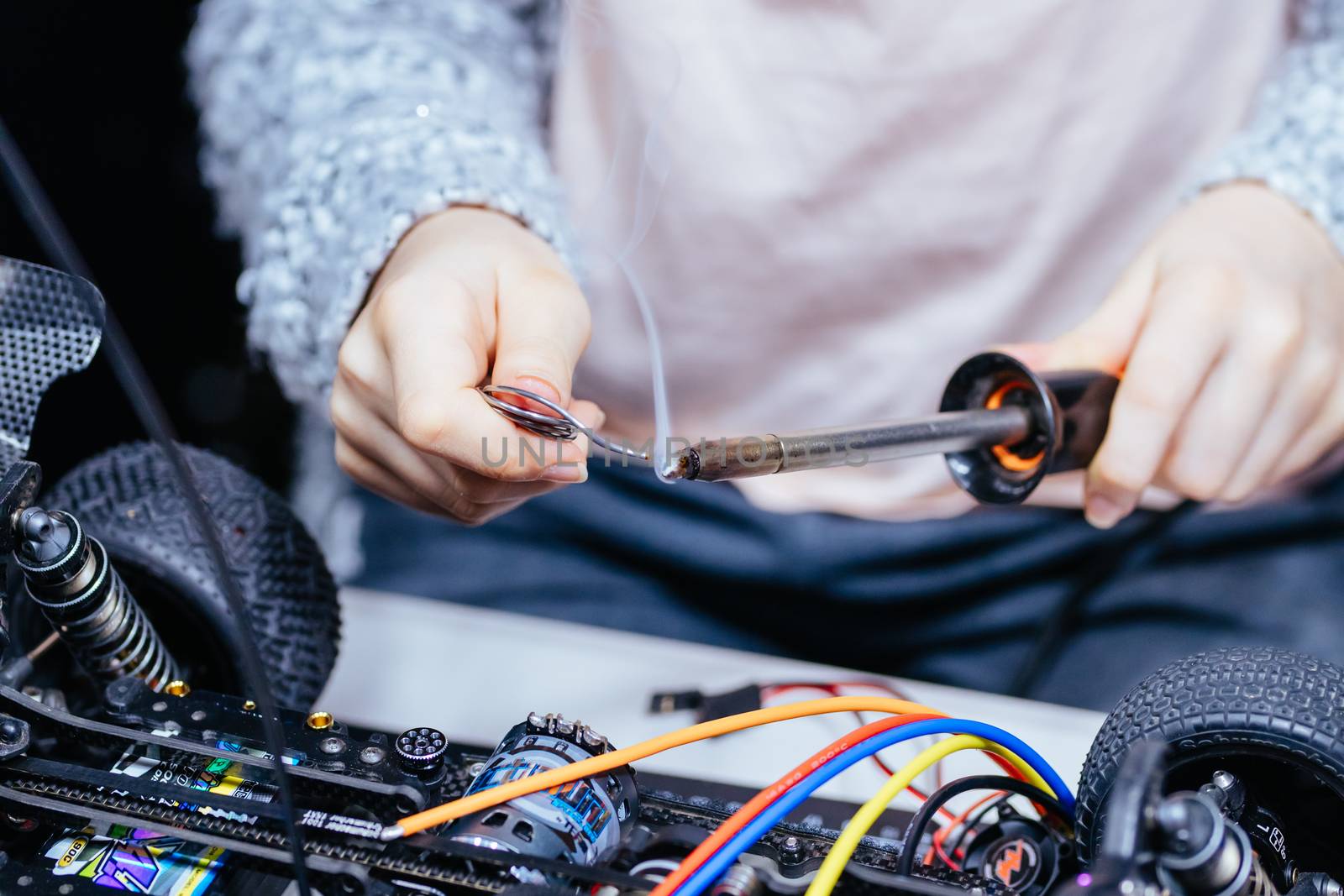 A young girl learns how to solder and is attaching an ESC to a motor in an RC car at a home workshop