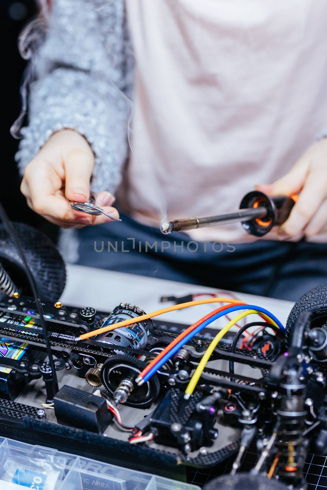 A young girl learns how to solder and is attaching an ESC to a motor in an RC car at a home workshop