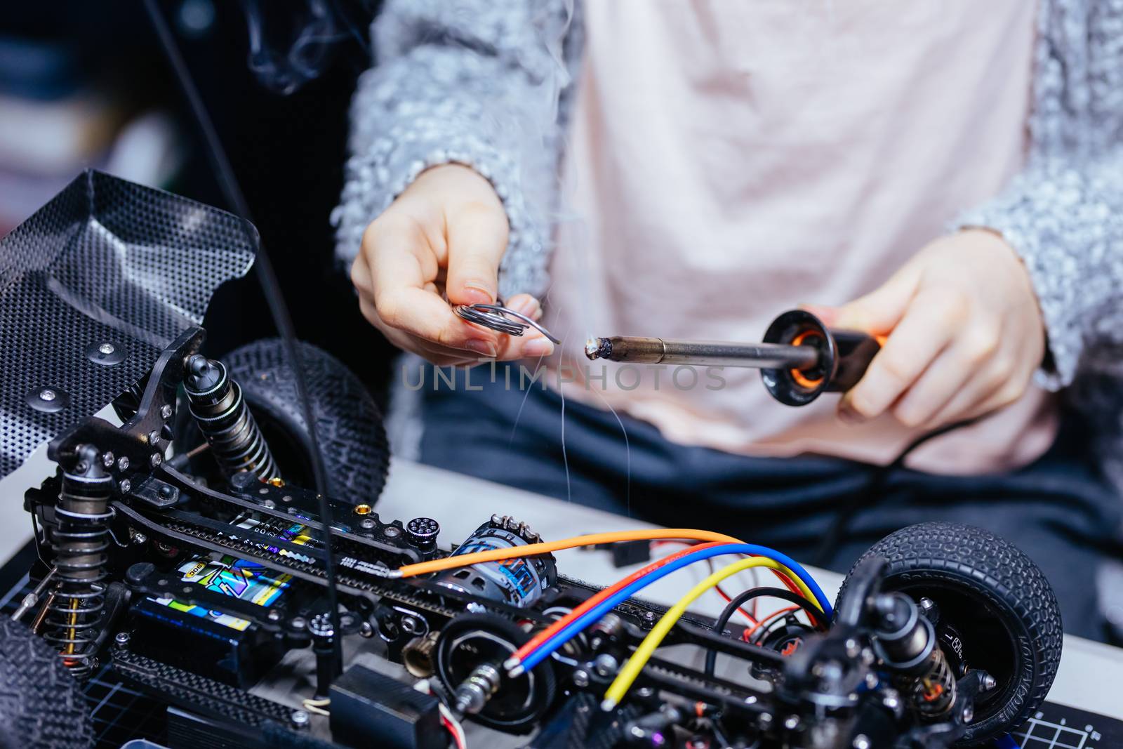 A young girl learns how to solder and is attaching an ESC to a motor in an RC car at a home workshop