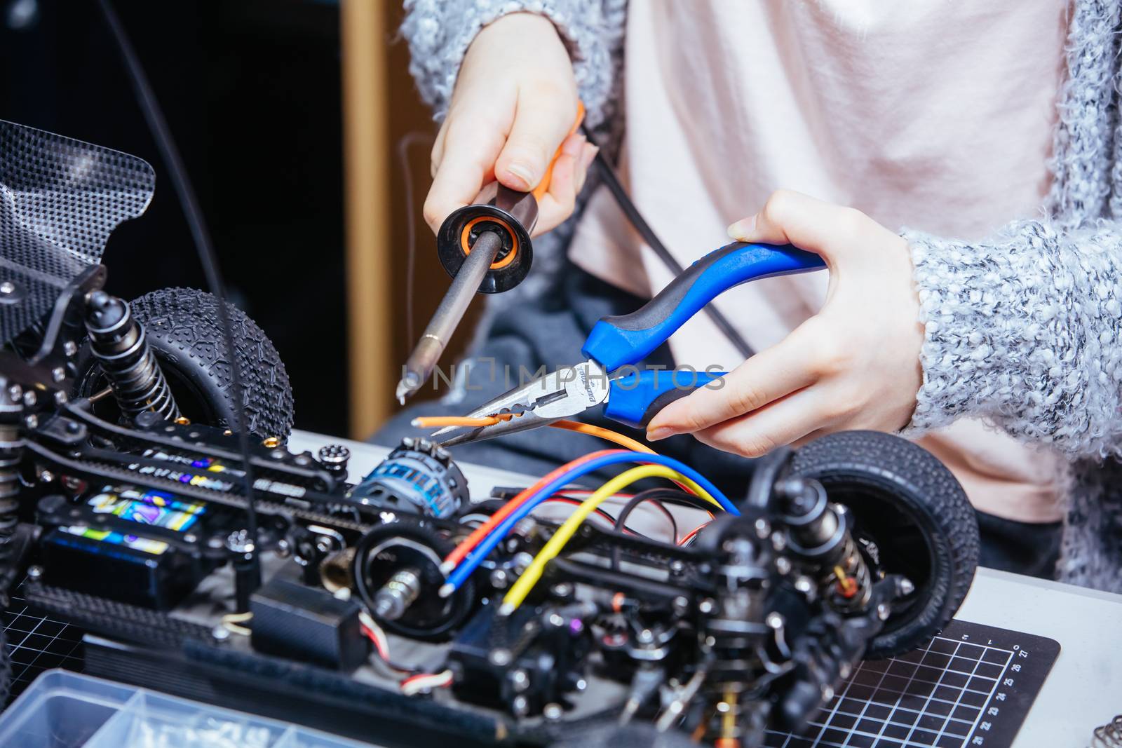 A young girl learns how to solder and is attaching an ESC to a motor in an RC car at a home workshop