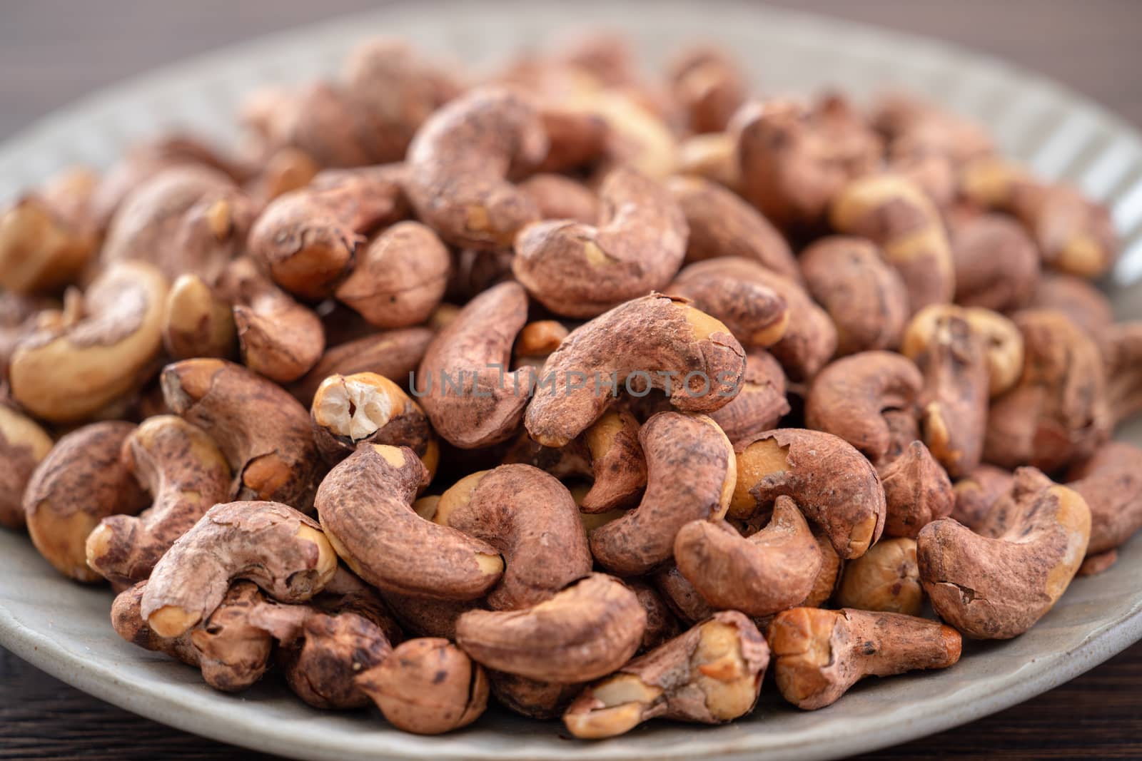Cashew nuts with peel in a plate on wooden tray and table background, healthy raw food concept.