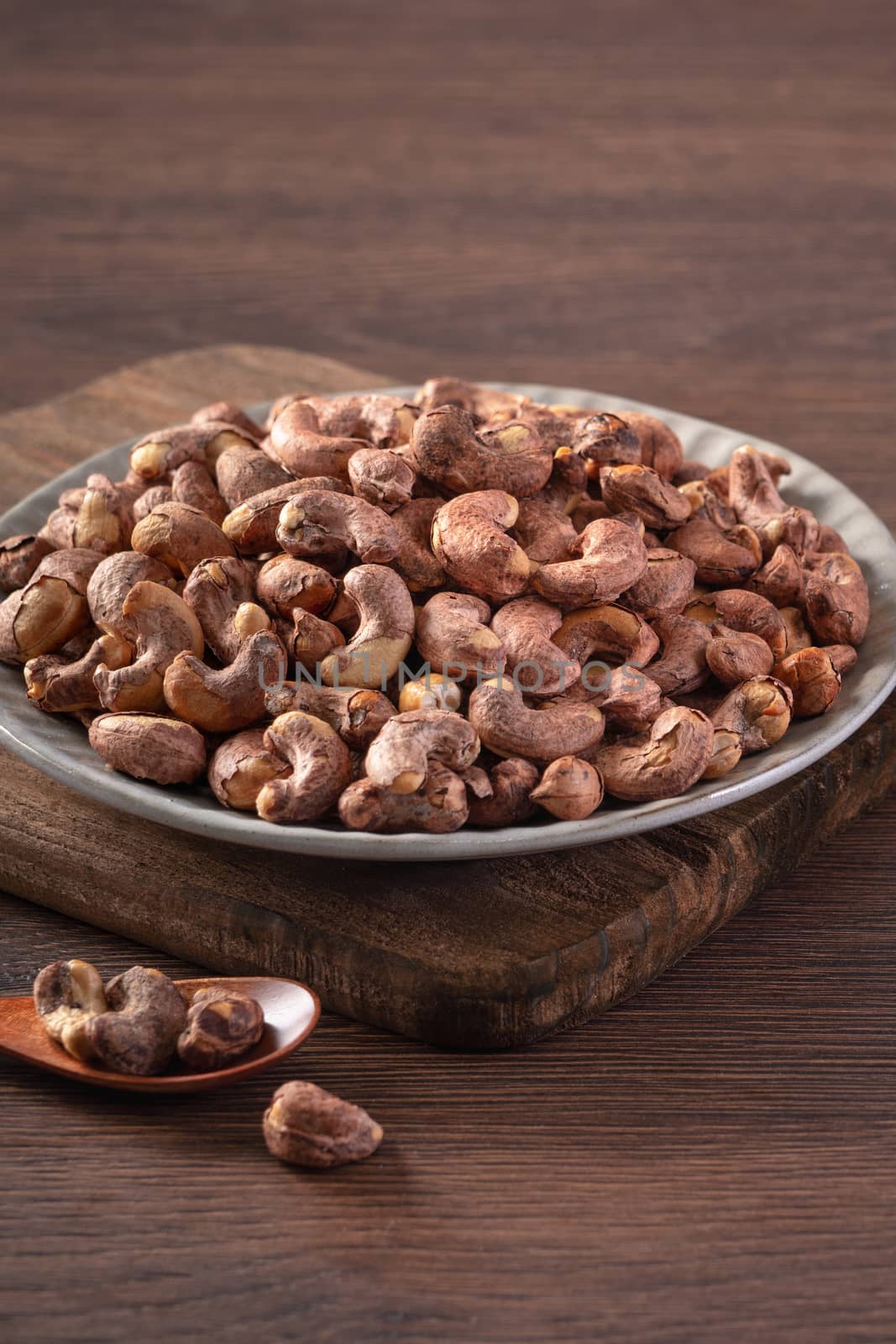 Cashew nuts with peel in a plate on wooden tray and table background, healthy raw food concept.