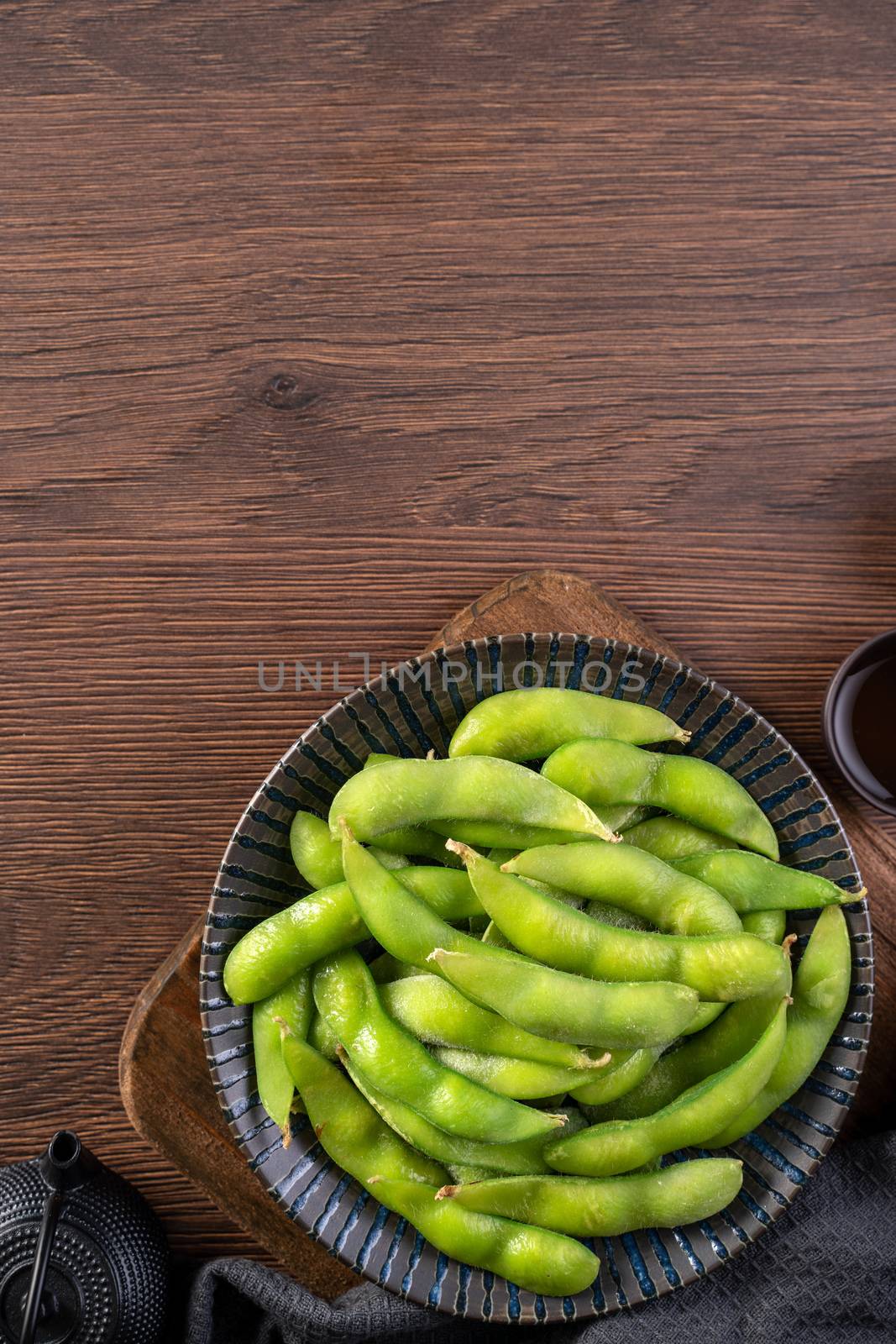 Fresh cooked boiled edamame in a plate on wooden tray and table background, healthy protein food concept.