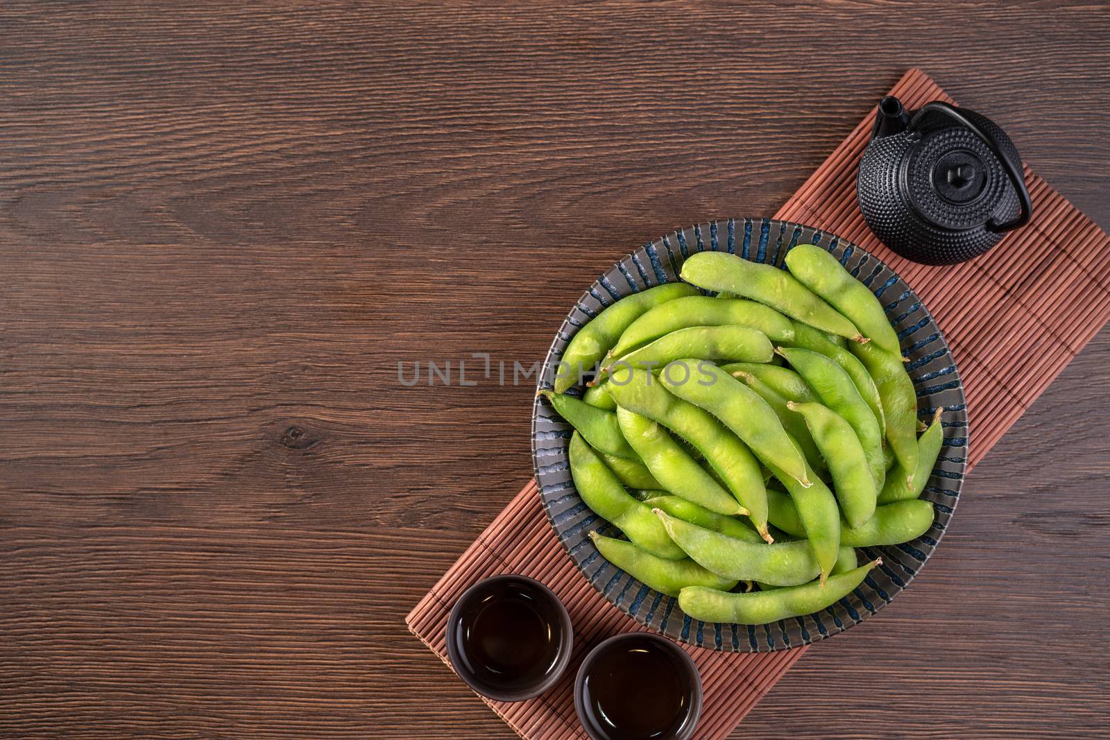 Fresh cooked boiled edamame in a plate on wooden tray and table background, healthy protein food concept.
