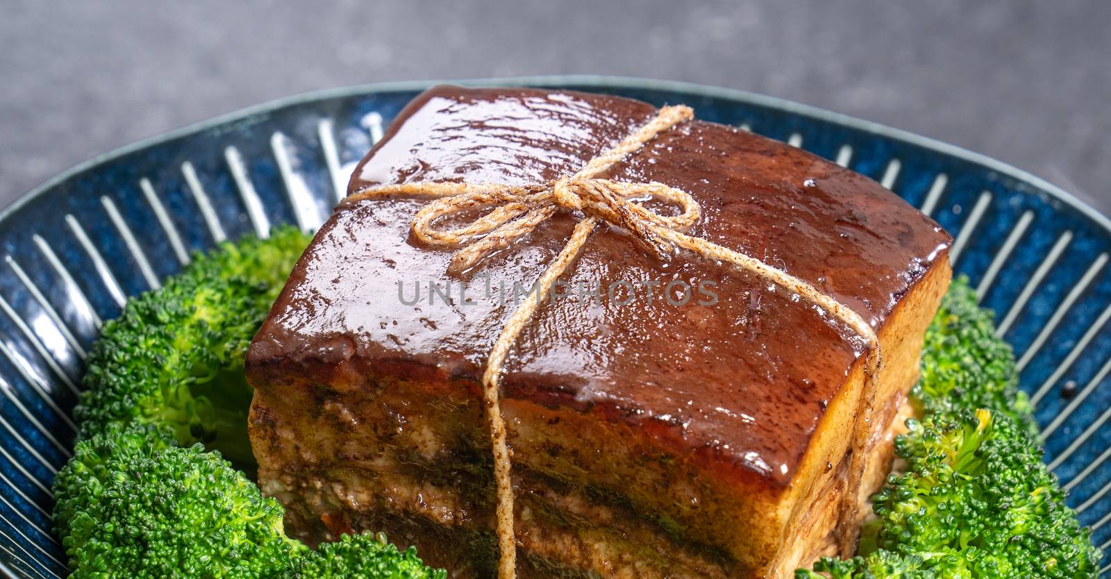 Dong Po Rou (Dongpo pork meat) in a beautiful plate with green vegetable, traditional festive food for Chinese new year cuisine meal, close up.