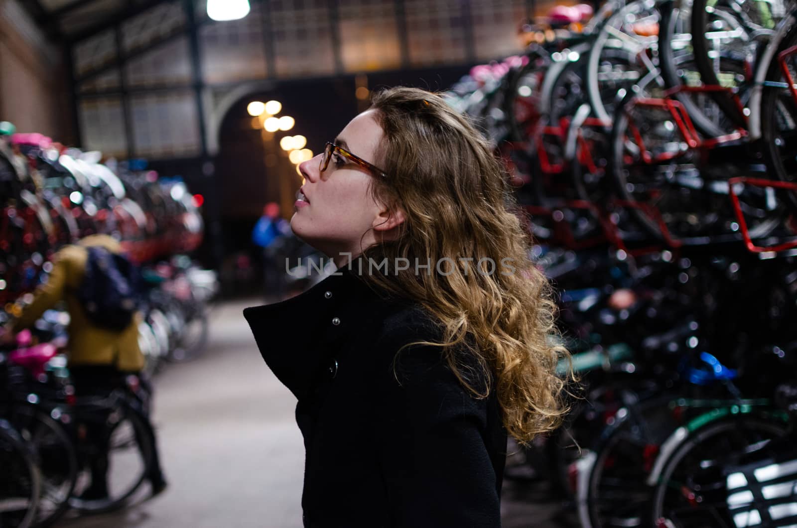 Photograph of a Spanish blonde girl dressed in black walking through the winter streets of a Dutch town in a bicycle parking lot.