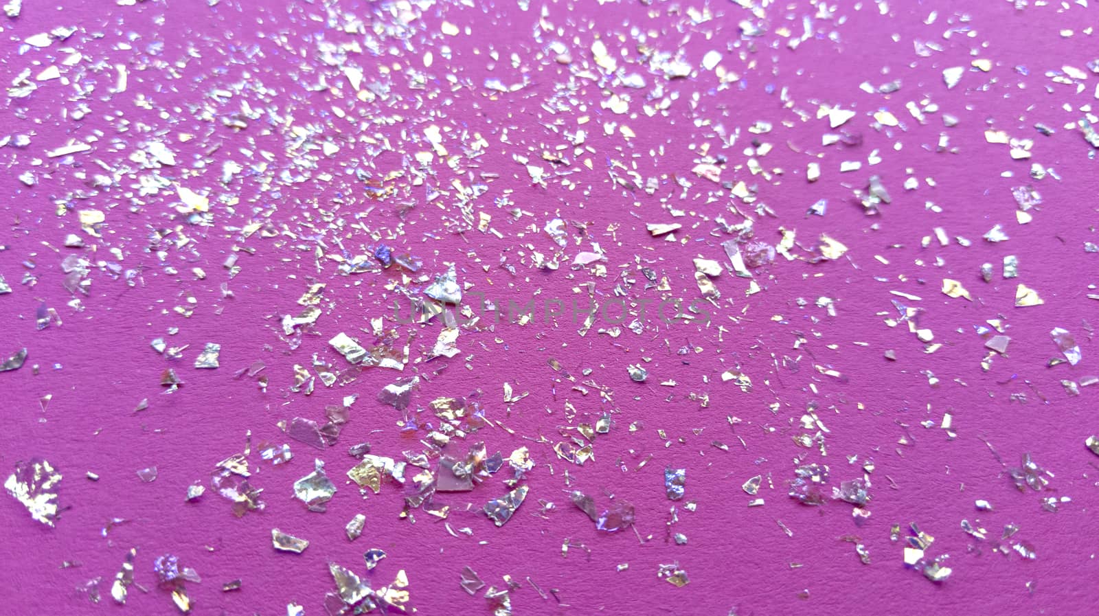 Foil pieces on pink background with multi-colored shine. Abstract fashion macro photo.